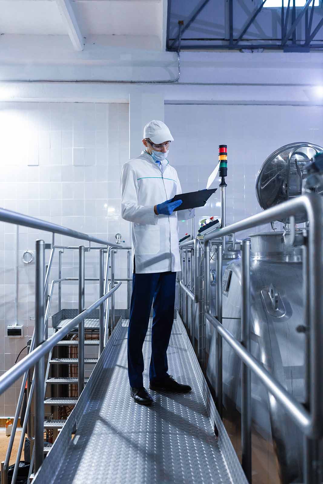 Inspector in a mask and a scrub stands with a folder-tablet in his hands at the dairy plant